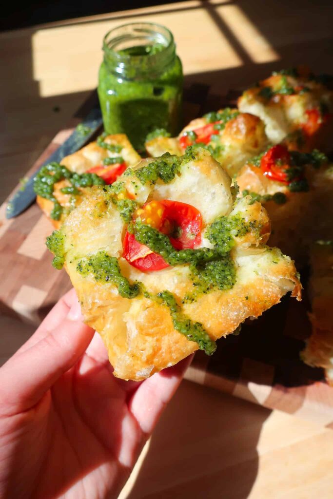 holding piece of basil pesto focaccia bread